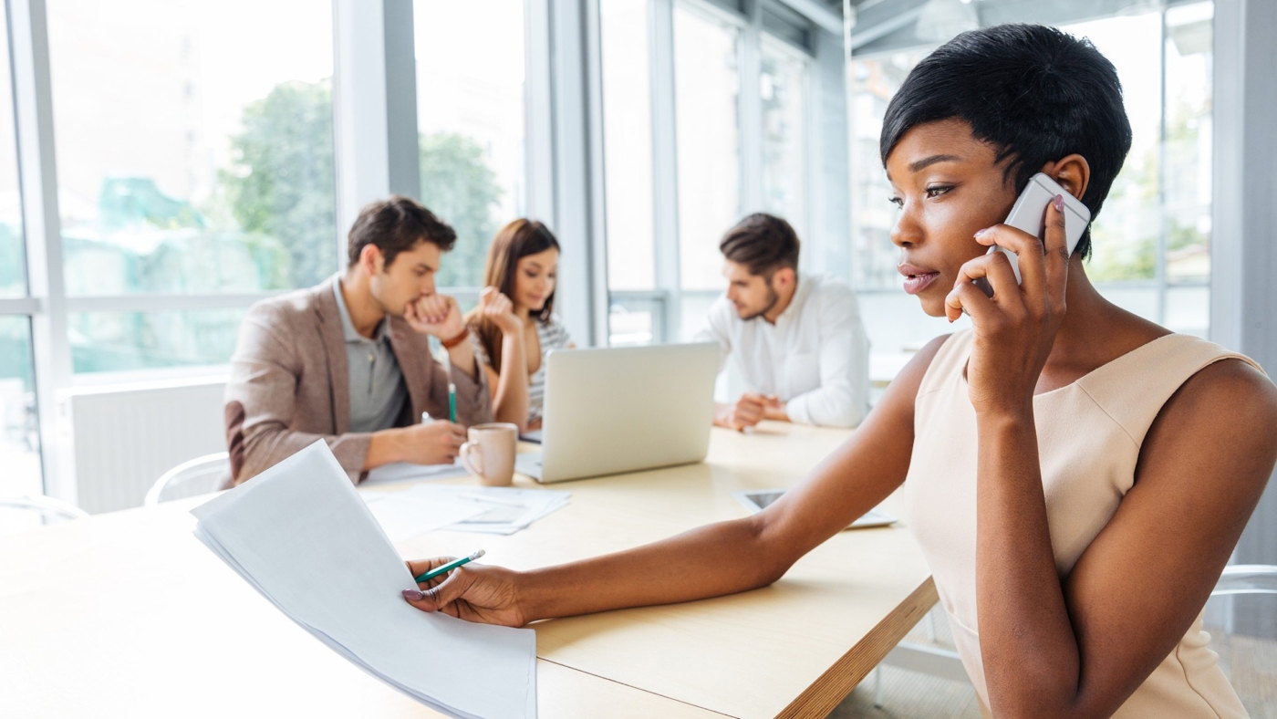 Serious businesswoman with documents talking on cell phone in office